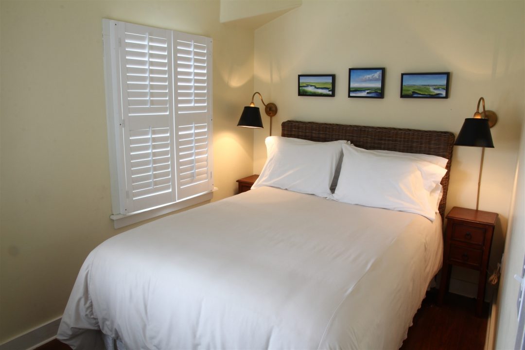 Second bedroom with queen bed, two bedside lamps, white blinds and local photography on wall